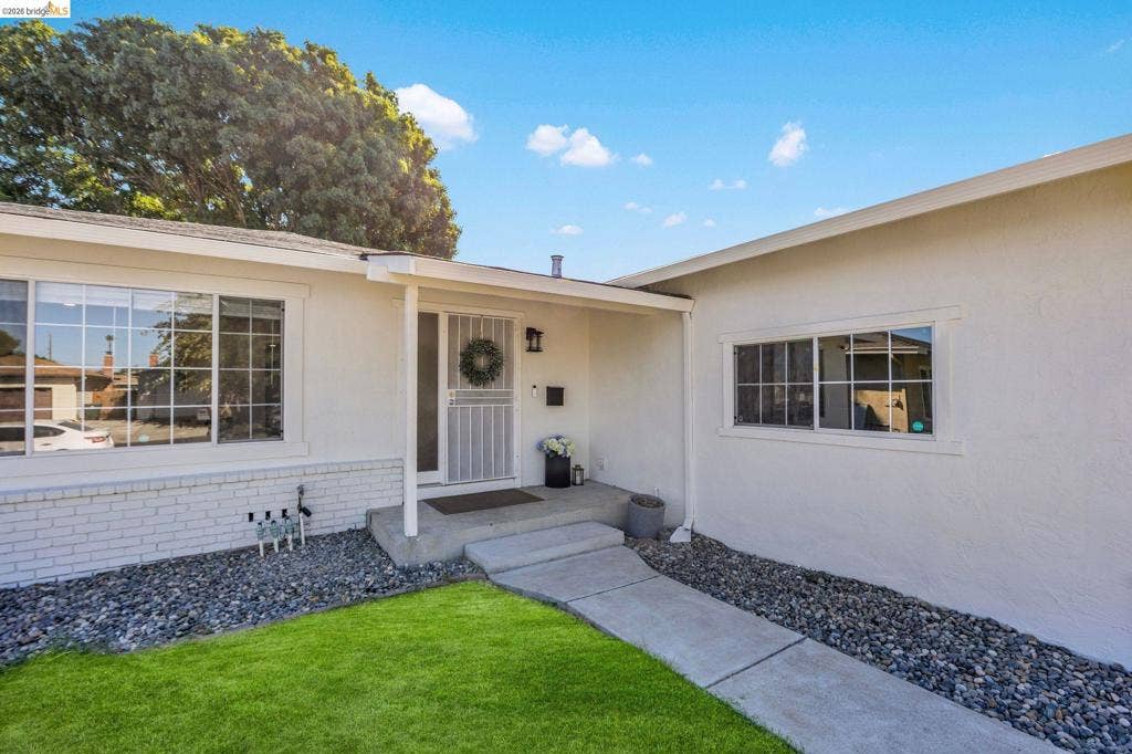 1509 Poppy Way, Antioch, CA 94509 White stucco exterior with a brick foundation, concrete walkway, and a landscaped front yard featuring green grass and decorative stone