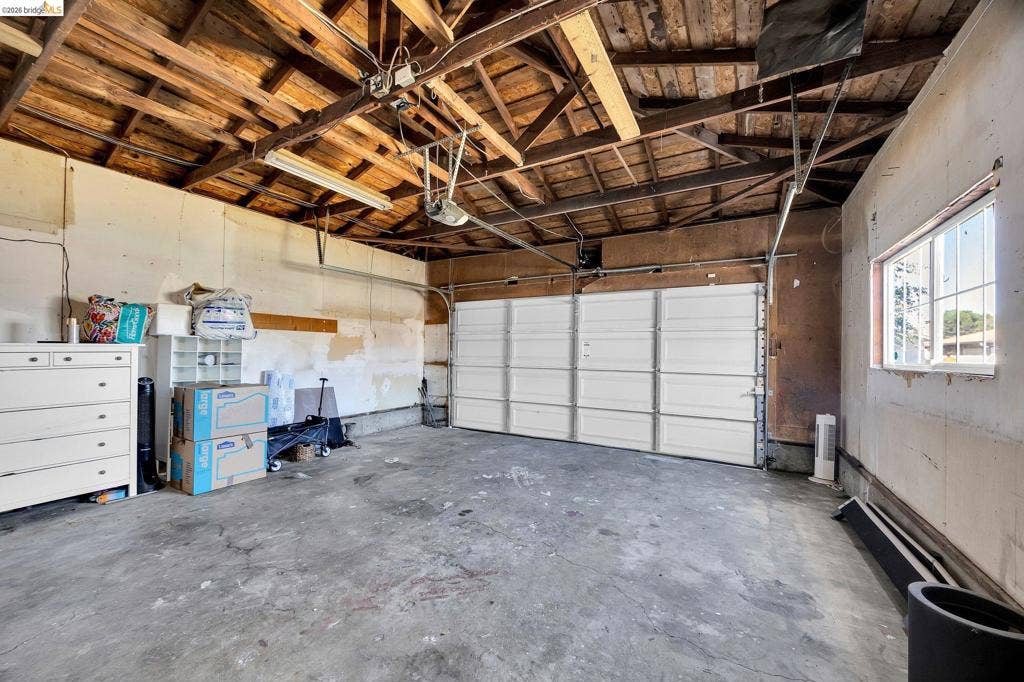 1509 Poppy Way, Antioch, CA 94509 Exposed wood beam ceiling, concrete flooring, overhead garage door, and natural light from window