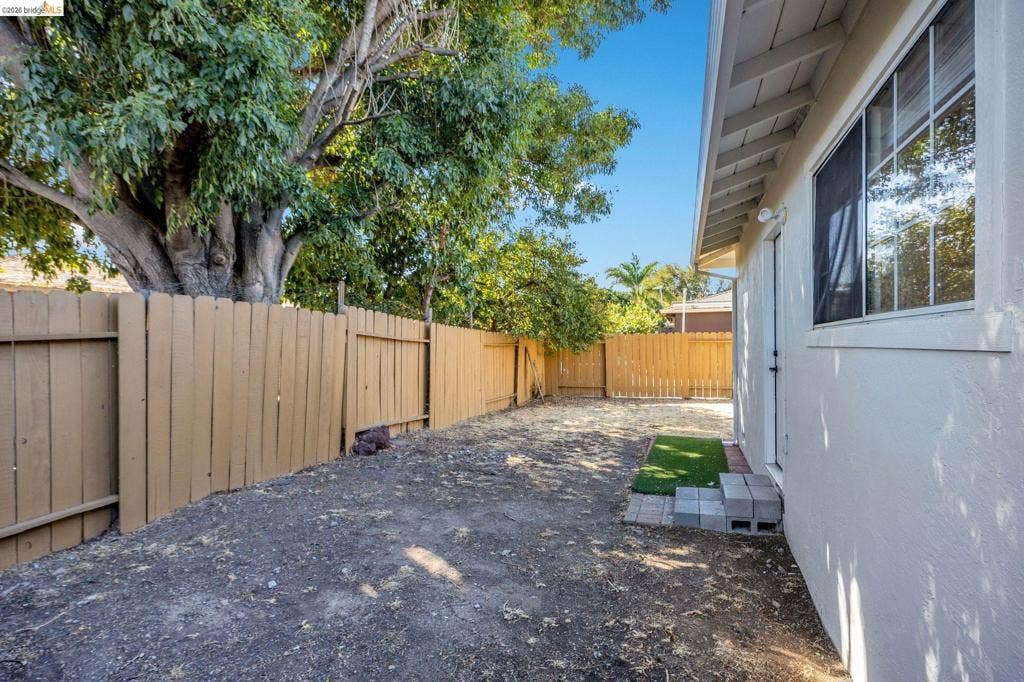 1509 Poppy Way, Antioch, CA 94509 Rear yard area featuring a perimeter wood fence, mature trees, and a building exterior with a window