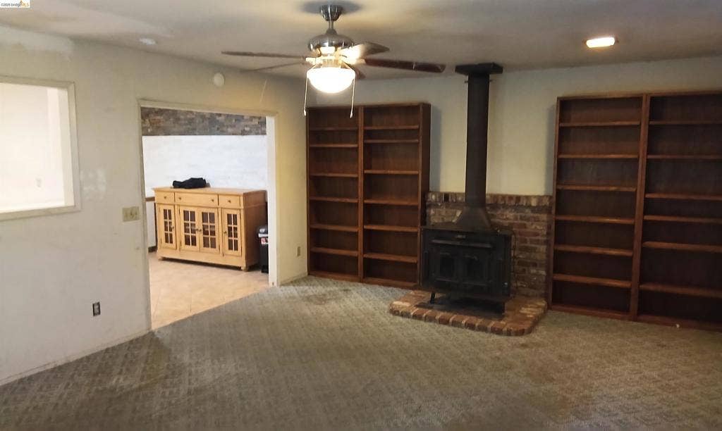 145 Viking Way, Pittsburg, CA 94565 Wood-burning stove with a brick hearth, two built-in wooden bookshelves, and a ceiling fan with integrated lighting