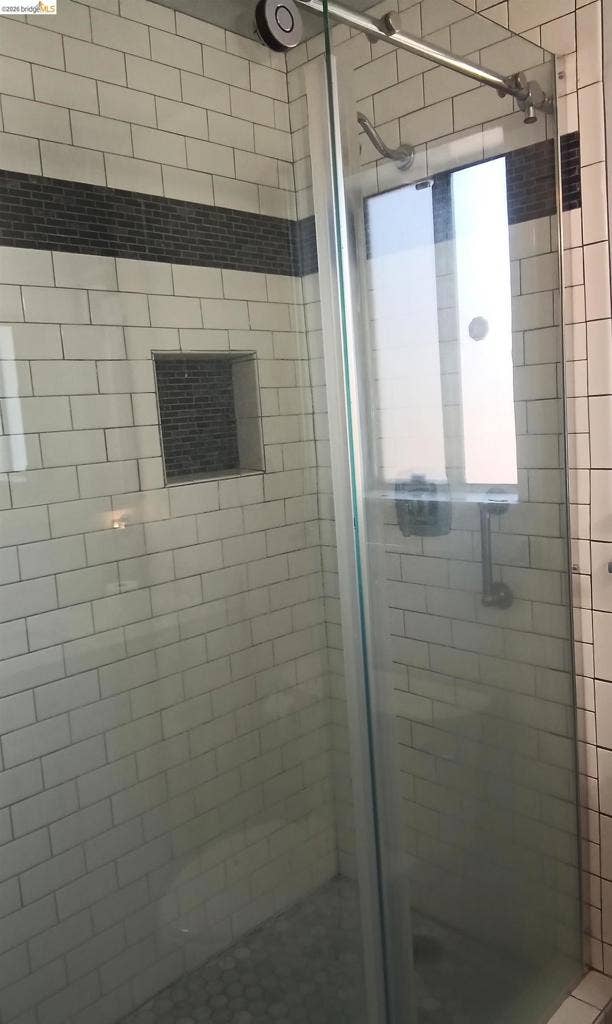 145 Viking Way, Pittsburg, CA 94565 Shower enclosure featuring white subway tile, a dark mosaic tile accent band, a built-in shower niche, a sliding glass door, and a pebble-finish shower floor