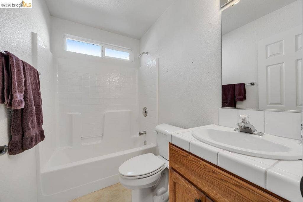 981 Country Ln, Angels Camp, CA 95222 White bathtub with integrated shower, transom window, and a tile-surround vanity with wood-finish cabinetry