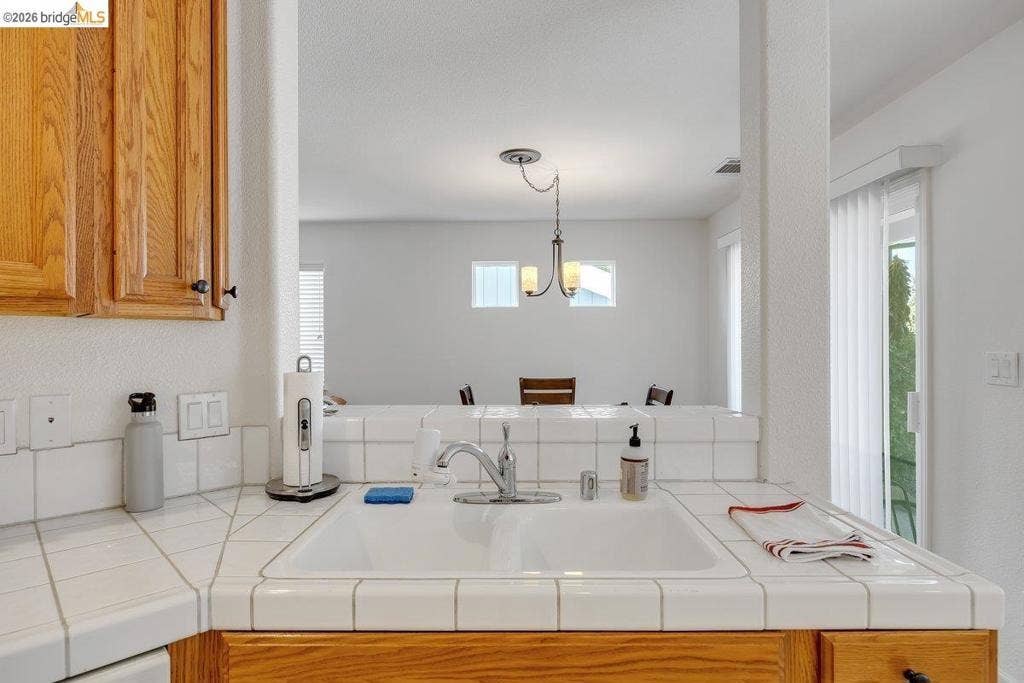 981 Country Ln, Angels Camp, CA 95222 Kitchen with tile countertops, a single basin sink, wood-finish cabinetry, and a pass-through opening