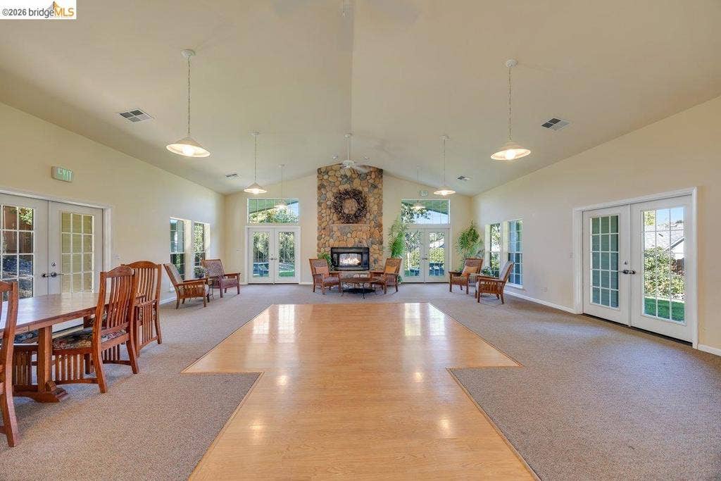 981 Country Ln, Angels Camp, CA 95222 Vaulted ceiling with pendant lighting, central wood-finish flooring, stone-clad fireplace, and multiple French doors