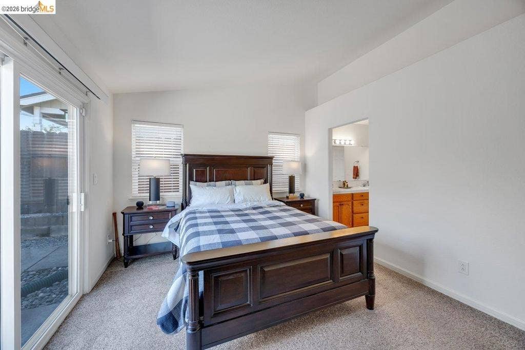 981 Country Ln, Angels Camp, CA 95222 Vaulted ceiling, carpeted flooring, sliding glass door, two windows with blinds, and an attached bathroom with a wood-finish vanity