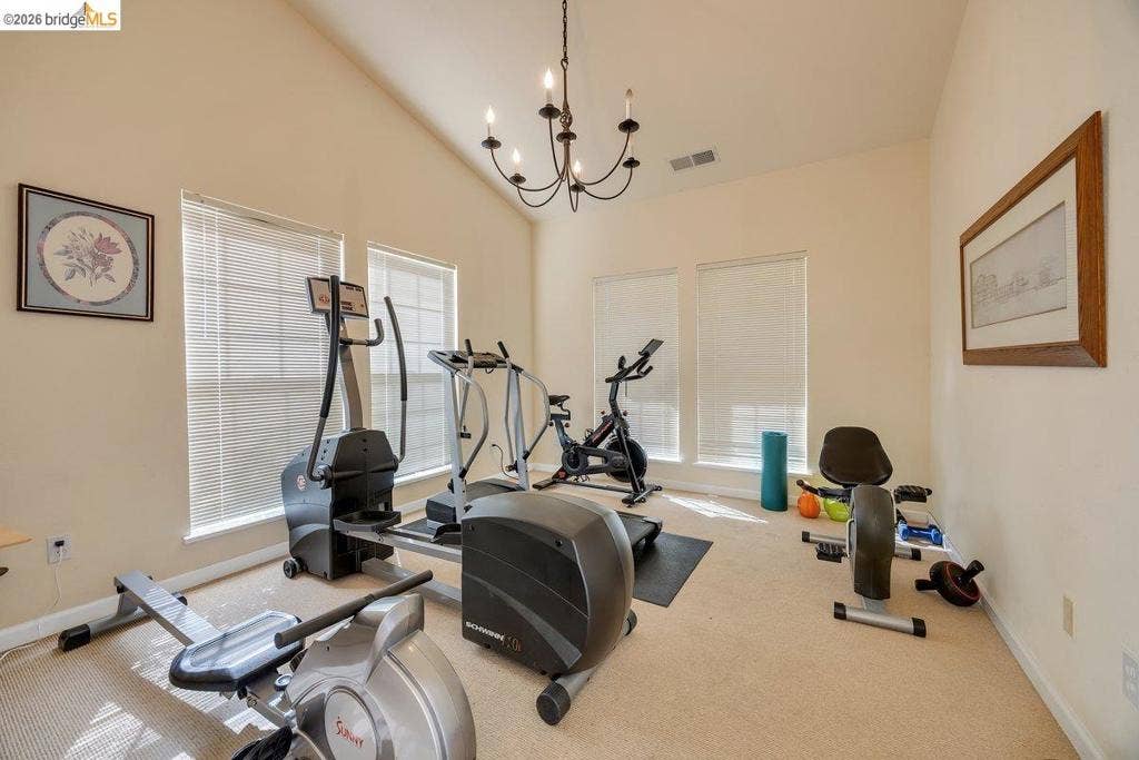981 Country Ln, Angels Camp, CA 95222 Dedicated fitness room featuring vaulted ceilings, abundant natural light from dual windows with plantation shutters, chandelier lighting, neutral carpet flooring, and space configured for multiple exercise stations