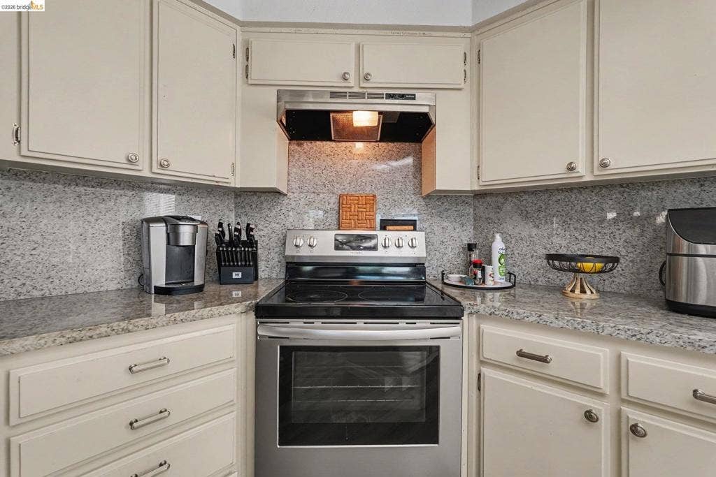 304 Greystone Dr, Antioch, CA 94509 Kitchen featuring light-toned cabinetry, stone-finish countertops, full-height stone-finish backsplash, and stainless steel freestanding range with an integrated hood