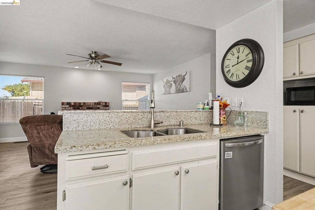 304 Greystone Dr, Antioch, CA 94509 Kitchen featuring light-toned countertops, double-basin stainless steel sink with high-arc faucet, stainless steel dishwasher, white cabinetry, and wood-finish flooring