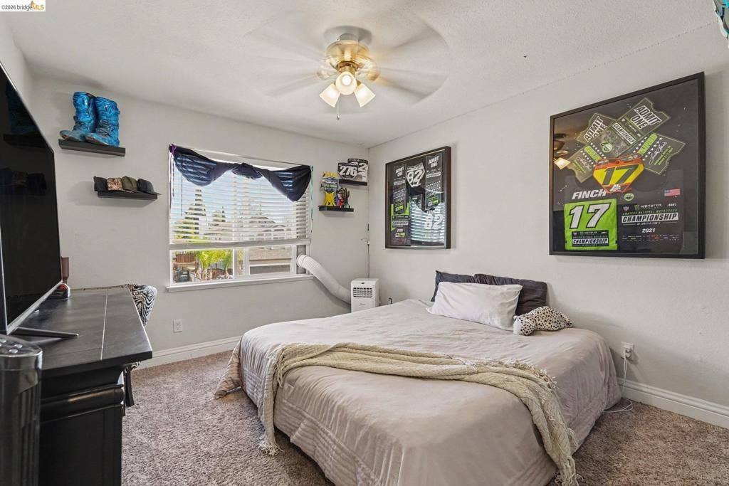 304 Greystone Dr, Antioch, CA 94509 Neutral-toned interior space featuring wall-to-wall carpeting, an integrated ceiling fan with multi-light fixture, a double-pane horizontal sliding window, and fixed wall-mounted shelving