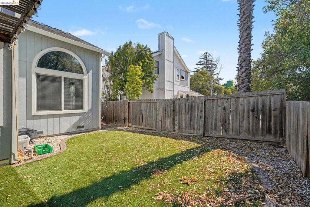 304 Greystone Dr, Antioch, CA 94509 Exterior space featuring vertical wood-style siding, a large arched window, synthetic turf lawn, rock landscaping, and a wood privacy fence