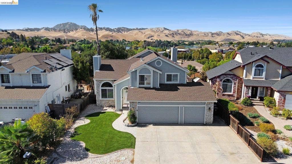 304 Greystone Dr, Antioch, CA 94509 Two-story residence featuring a shingled roof, stone veneer accents, an attached three-car garage, solar panels, and a manicured front lawn set against a mountainous backdrop