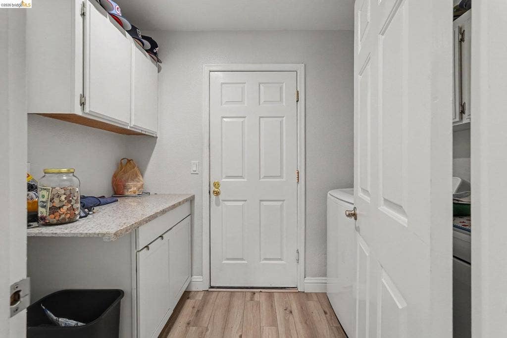 304 Greystone Dr, Antioch, CA 94509 Laundry room featuring wood-finish flooring, white cabinetry, light-toned stone-finish countertops, and a six-panel exterior door