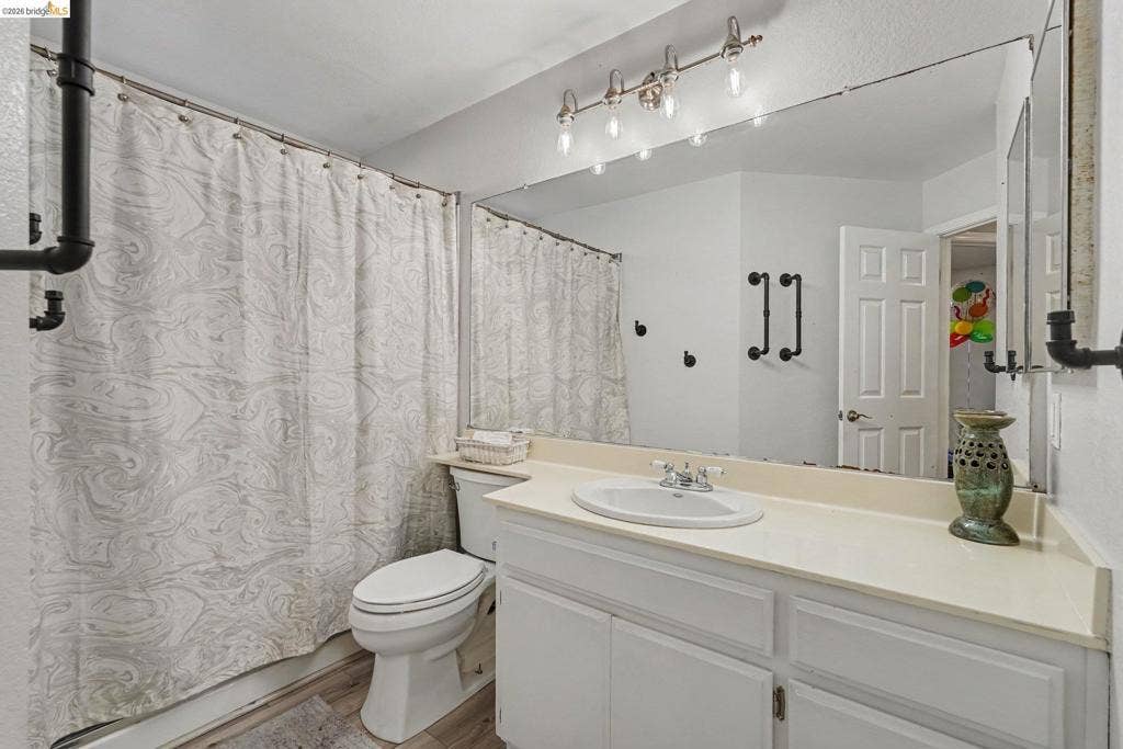 304 Greystone Dr, Antioch, CA 94509 Bathroom featuring white vanity cabinetry, integrated countertop with a recessed basin, full-width wall mirror, industrial-style multi-light fixture, and matte black hardware