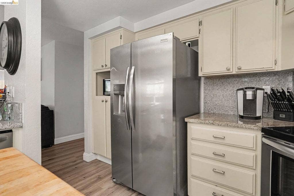 304 Greystone Dr, Antioch, CA 94509 Kitchen featuring stainless steel side-by-side refrigerator, speckled stone countertops, light-toned cabinetry, and wood-finish flooring