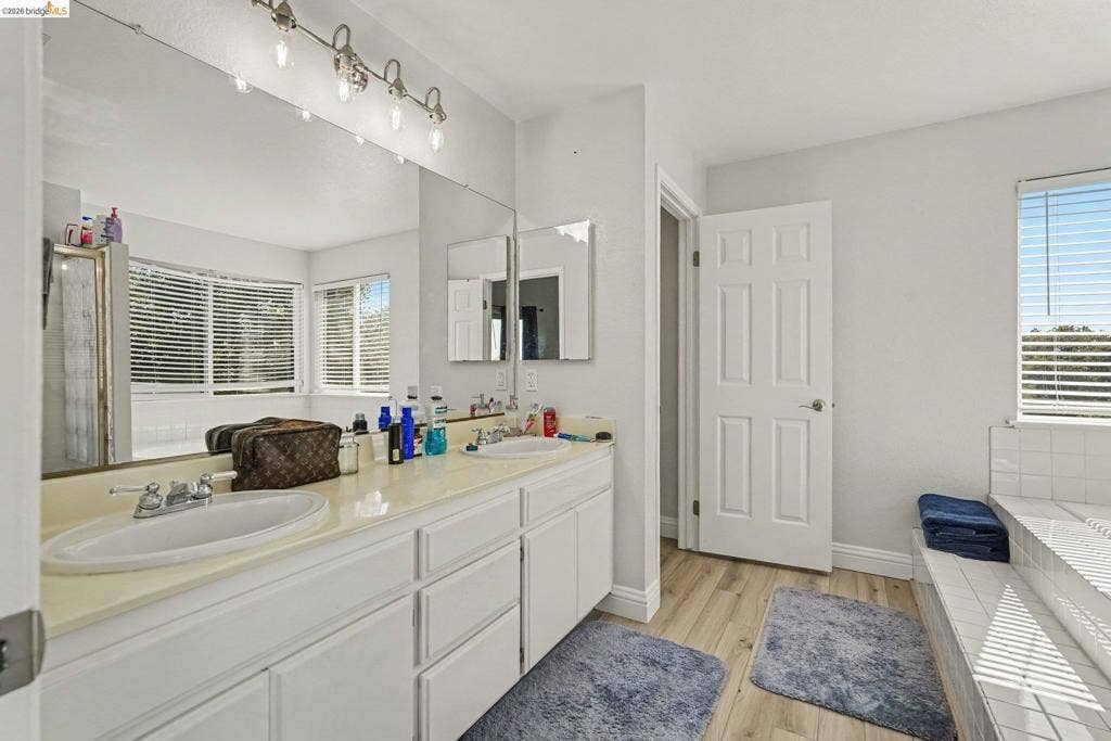 304 Greystone Dr, Antioch, CA 94509 Double vanity featuring a wide countertop, recessed sink basins, full-width vanity mirror, and wood-finish flooring