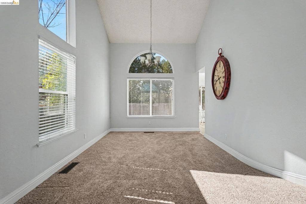 304 Greystone Dr, Antioch, CA 94509 Vaulted ceiling featuring a central chandelier, expansive windows, an arched window element, and wall-to-wall carpeting