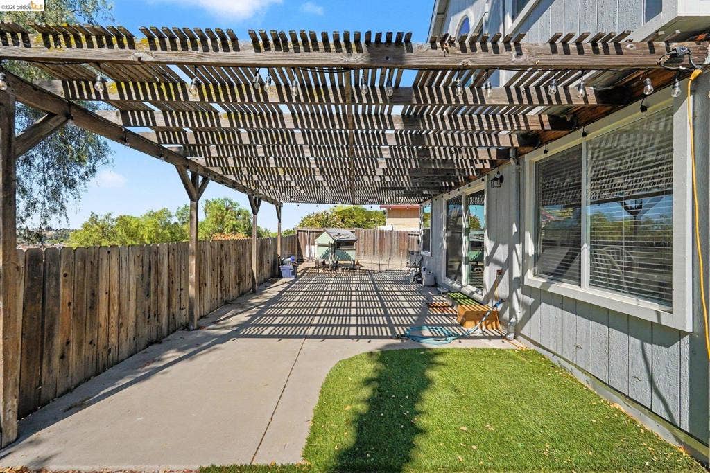 304 Greystone Dr, Antioch, CA 94509 Backyard patio featuring a wood-slat pergola, concrete surfacing, synthetic turf, and a wood privacy fence