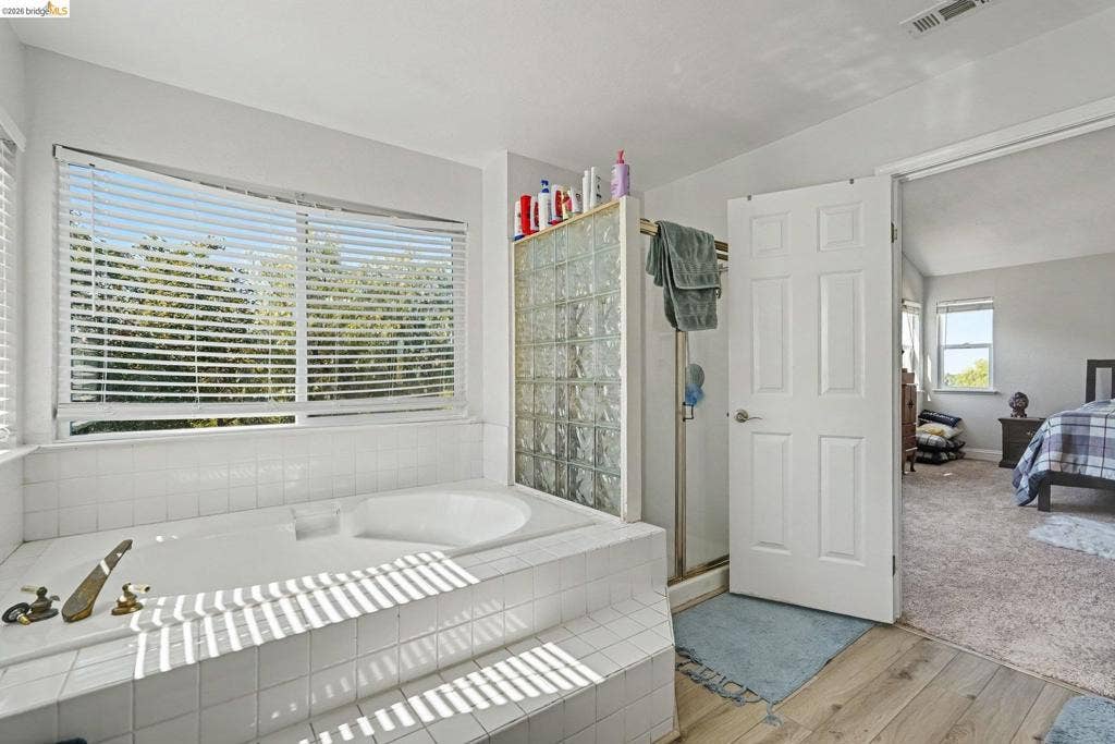304 Greystone Dr, Antioch, CA 94509 Built-in soaking tub with a tiled surround, glass block privacy partition, wood-finish flooring, and multi-panel interior door