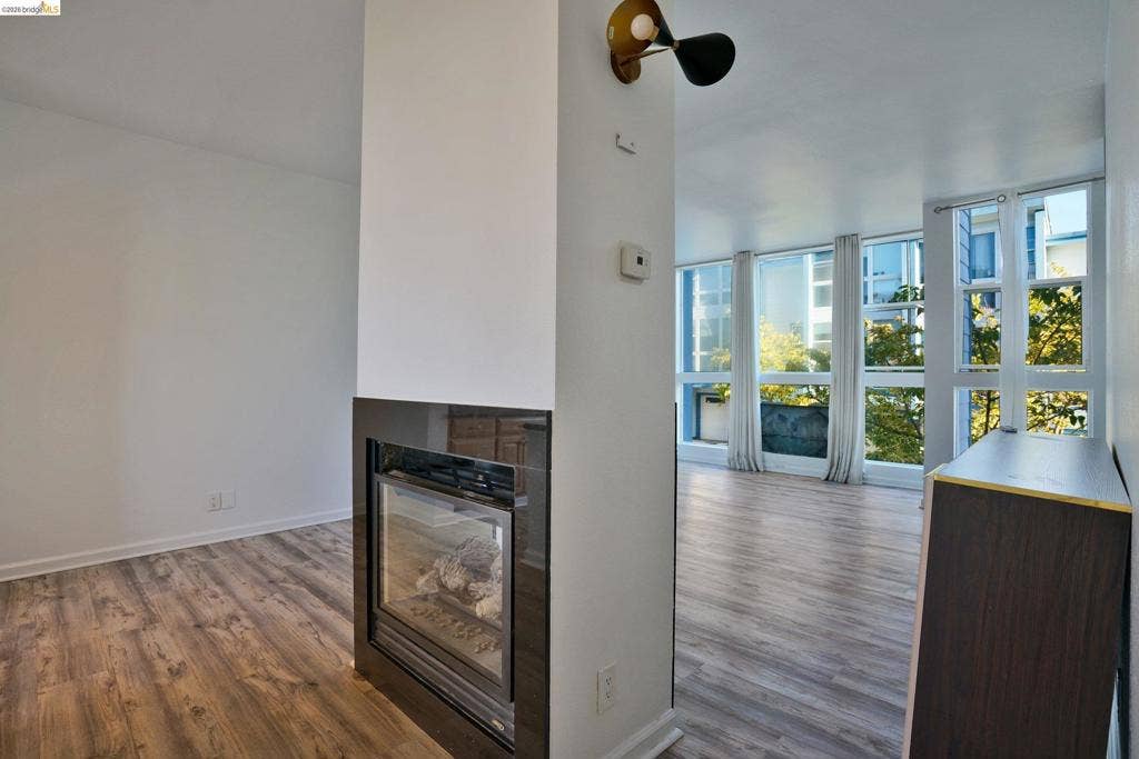Double-sided fireplace with a sleek dark tile surround, floor-to-ceiling windows, wood-finish flooring, and a multi-directional wall-mounted light fixture