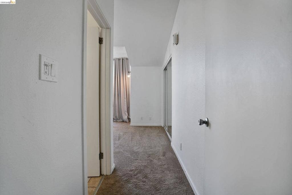 Interior hall featuring neutral carpeting, sliding mirrored closet doors, and smooth-finish white walls