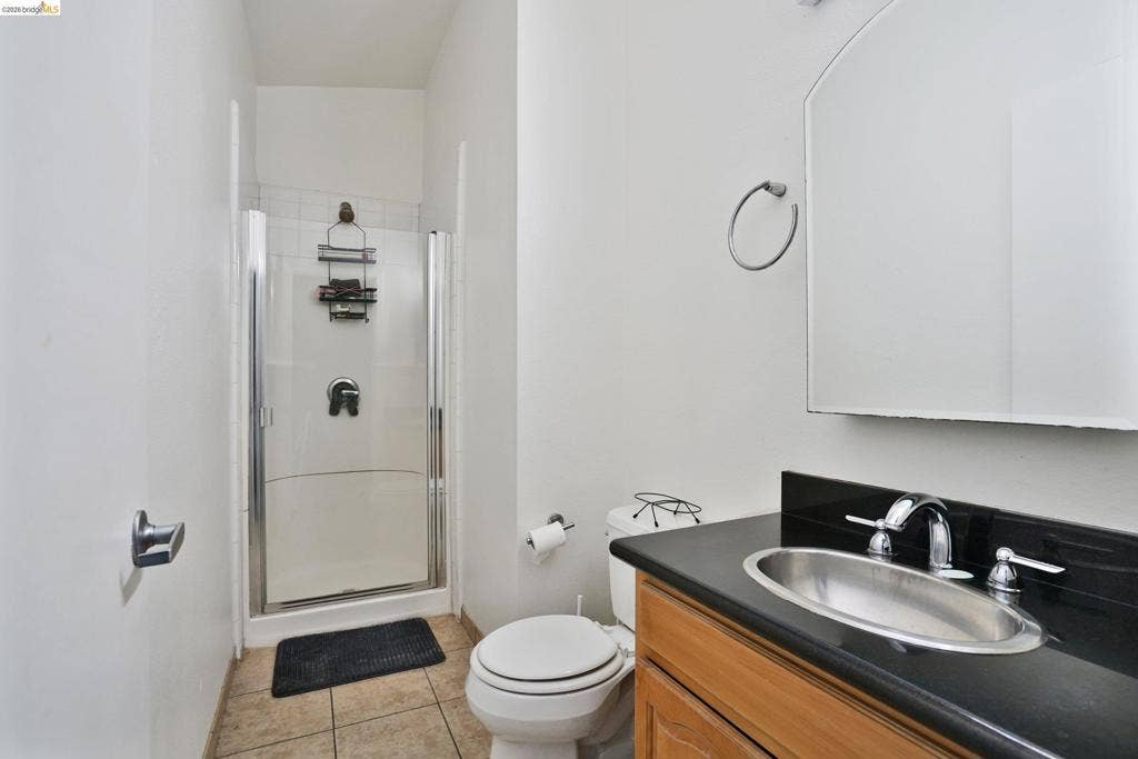 Bathroom featuring a walk-in shower with a glass enclosure, wood-finish vanity with a dark countertop, integrated metal sink, and an arched wall-mounted mirror