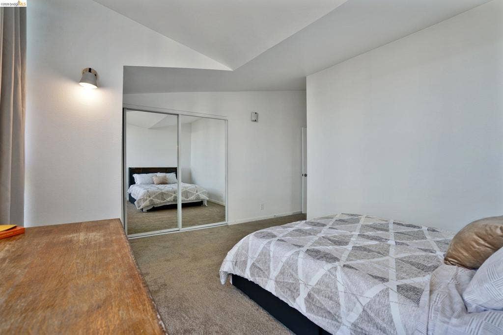 Vaulted ceiling featuring a wall-mounted light fixture and mirror-paneled sliding closet doors