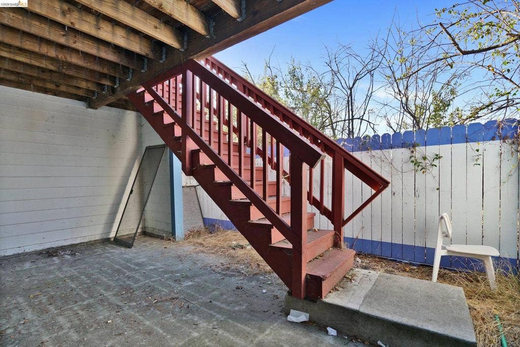 Covered patio featuring concrete flooring, an exposed timber ceiling, and exterior wooden staircase with matching railings