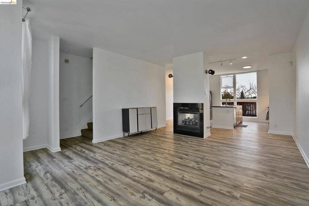 Open living area featuring wood-finish flooring, a double-sided fireplace with a black surround, track lighting, and floor-to-ceiling windows