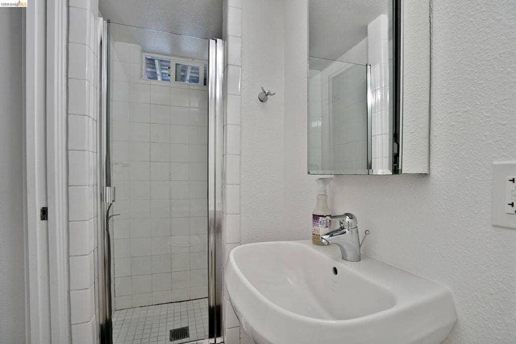 Wall-mounted white basin with chrome faucet, tiled shower stall with glass door, and recessed mirrored medicine cabinet