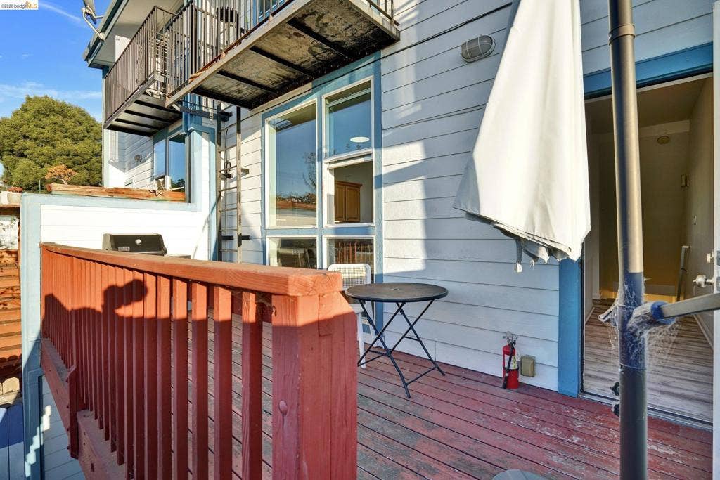 Exterior deck featuring painted wood-plank flooring, a wood railing, metal balcony stairs, and expansive multi-pane windows
