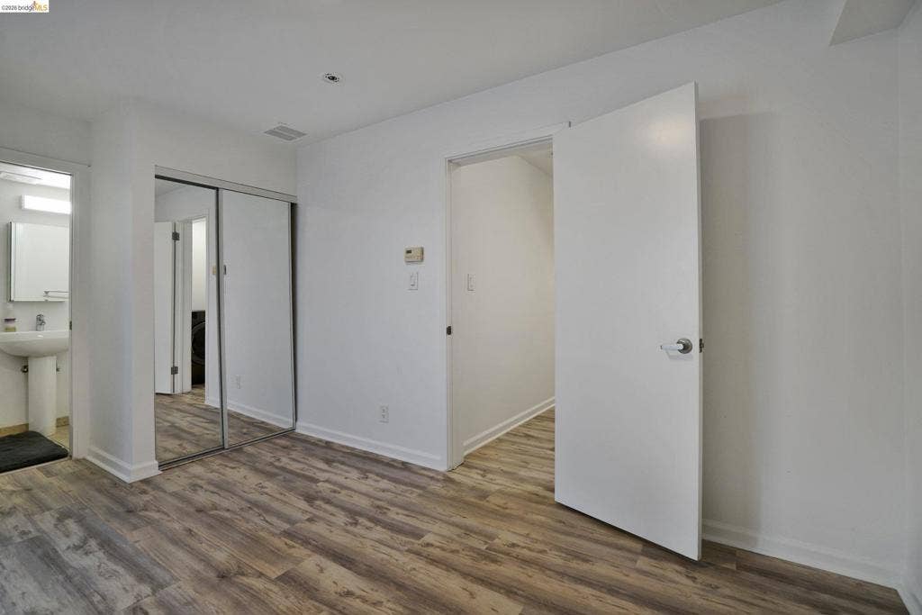 Wood-finish flooring, mirrored sliding closet doors, and pedestal sink with wall-mounted lighting
