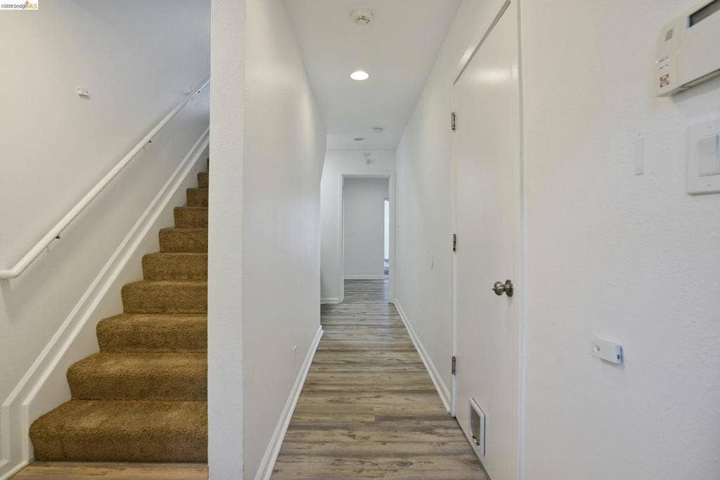 Hallway featuring wood-finish flooring, carpeted stairs with a white handrail, recessed lighting, and white interior doors