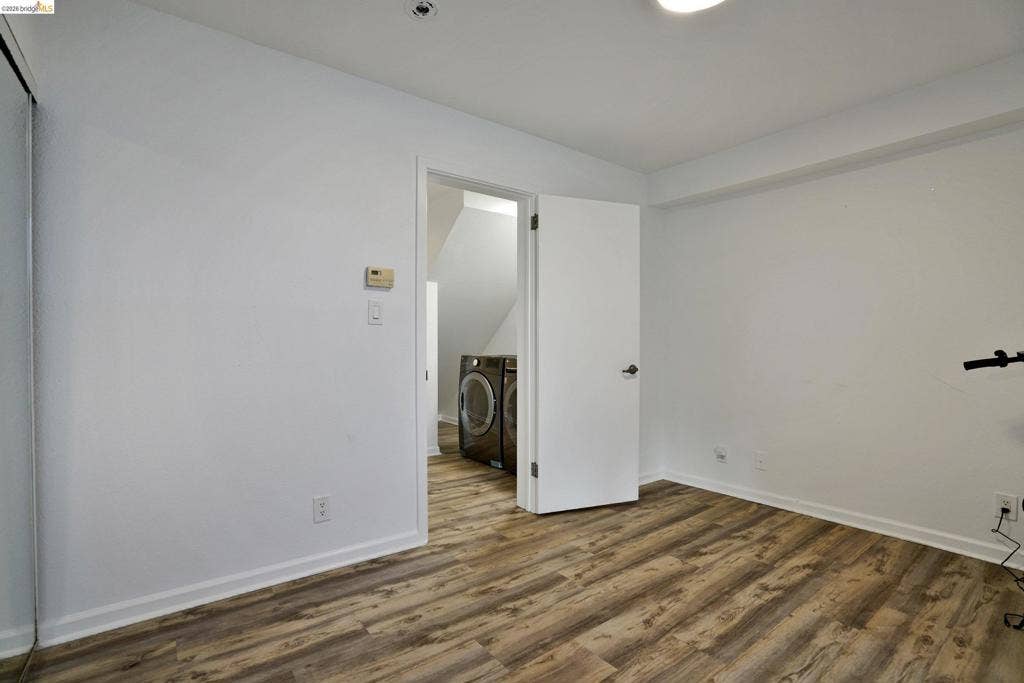 Neutral-toned room featuring wood-finish flooring, a sliding-door closet, and an interior door opening to a utility space