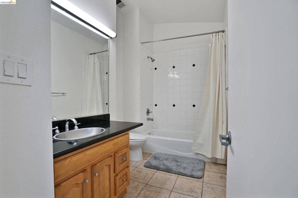 Bathroom featuring a wood vanity with a black countertop and integrated oval sink, full-width mirror with linear lighting, and a tub-shower combination with white tile surround and decorative accent insets