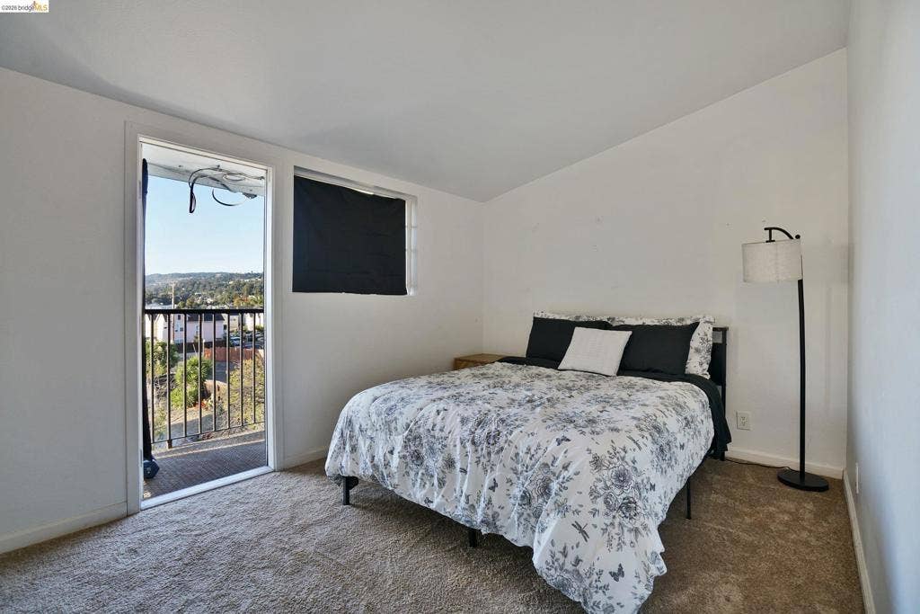 Neutral-toned wall-to-wall carpeting, single-pane window, and private exterior balcony with metal railing