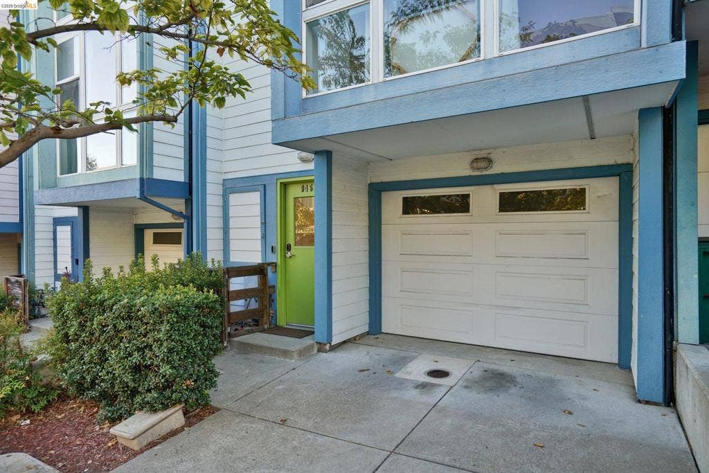 Multi-level exterior featuring white horizontal siding, contrasting blue trim, a private garage with a sectional door, and an entryway accented by a vibrant door
