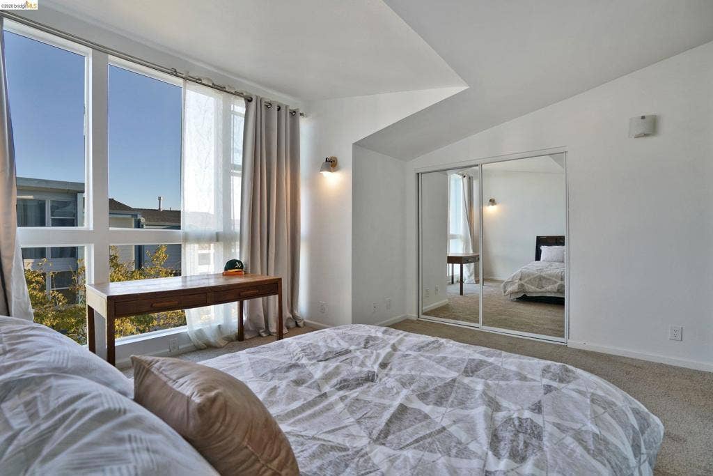 Floor-to-ceiling windows, vaulted ceiling, sliding mirrored closet doors, and wall-mounted sconce lighting