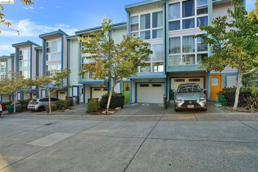 Multi-level townhome exterior featuring contemporary architectural design, expansive floor-to-ceiling windows, attached garage parking, and private concrete driveways