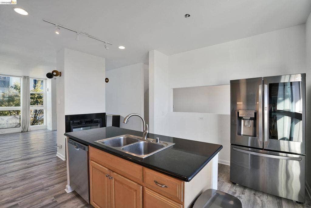 Kitchen featuring an island with a dual-basin stainless steel sink and dark countertop, wood-finish cabinetry, stainless steel appliances, and track lighting