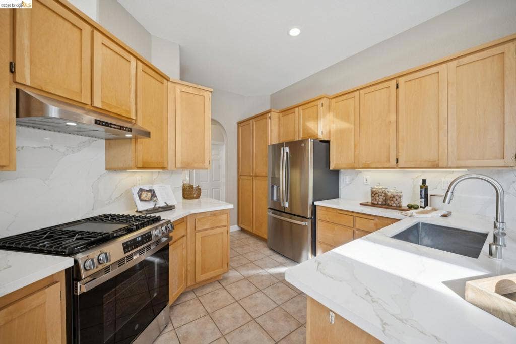 5503 Rainbow Cir, Santa Rosa, CA 95409 Kitchen featuring light wood cabinetry, quartz countertops, a full-height stone-pattern backsplash, stainless steel appliances, and a stainless steel undermount sink with a gooseneck faucet
