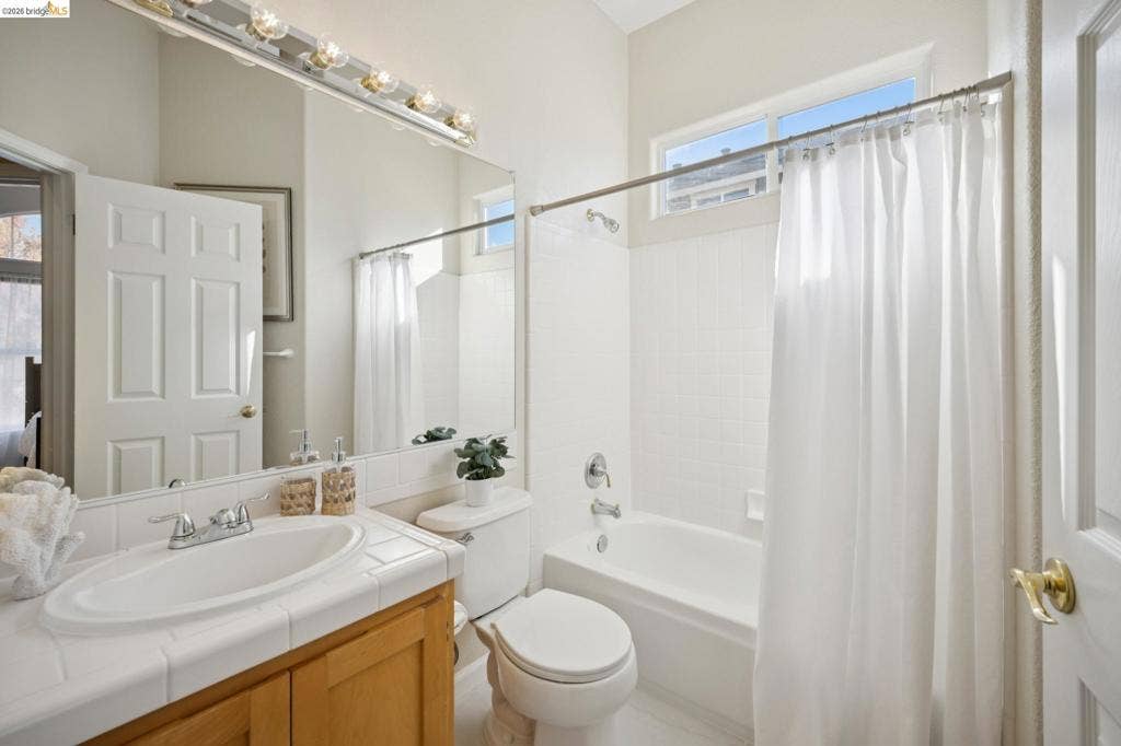 5503 Rainbow Cir, Santa Rosa, CA 95409 Bathroom featuring a tile-surround vanity, wooden cabinetry, a full-width wall mirror, and a tub-shower combination with tile surround and clerestory window