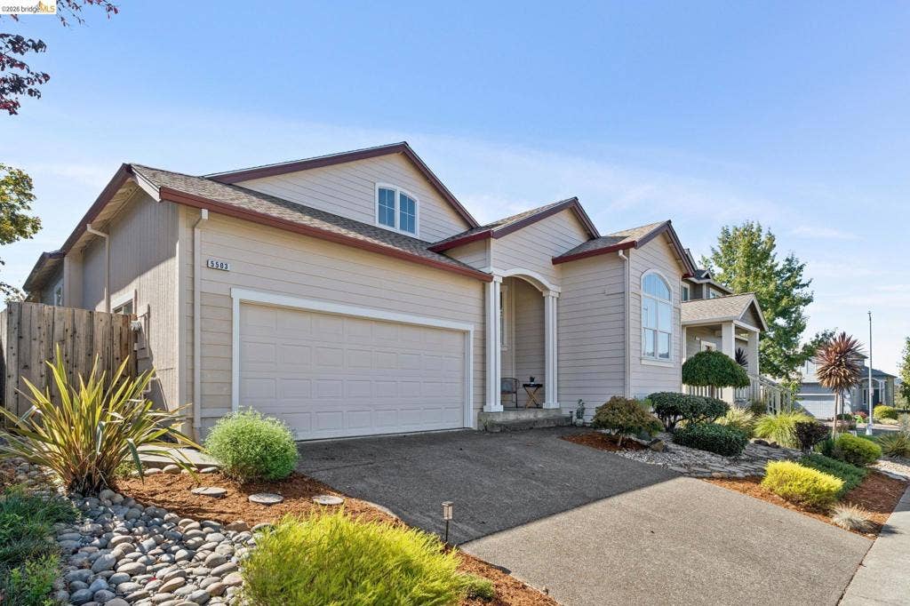 5503 Rainbow Cir, Santa Rosa, CA 95409 Exterior featuring horizontal lap siding, an arched entryway with column detailing, a multi-gabled roofline, an attached two-car garage, and landscaped rock garden beds