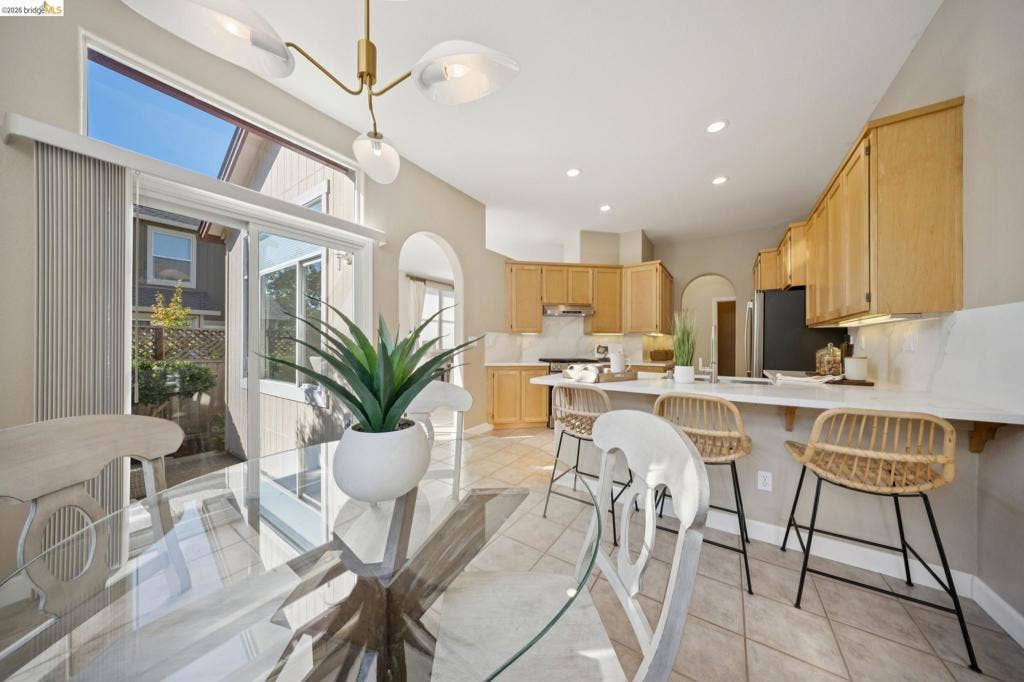 5503 Rainbow Cir, Santa Rosa, CA 95409 Open-concept kitchen featuring light wood cabinetry, white countertops, ceramic tile flooring, a multi-arm brass chandelier, and a sliding glass door with a transom window