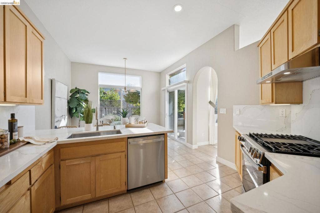 5503 Rainbow Cir, Santa Rosa, CA 95409 Kitchen featuring light wood cabinetry, white stone countertops, tile flooring, stainless steel appliances, and a prominent arched entryway