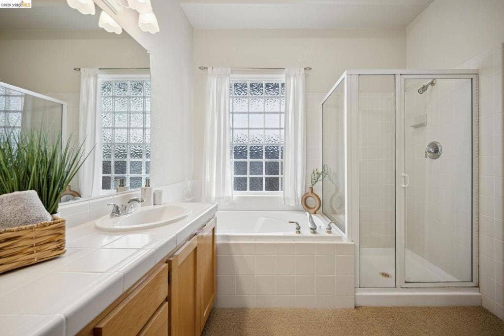 5503 Rainbow Cir, Santa Rosa, CA 95409 Bathroom featuring a tile-surround soaking tub, a glass-enclosed shower stall, a vanity with an integrated sink, and an expansive wall-mounted mirror