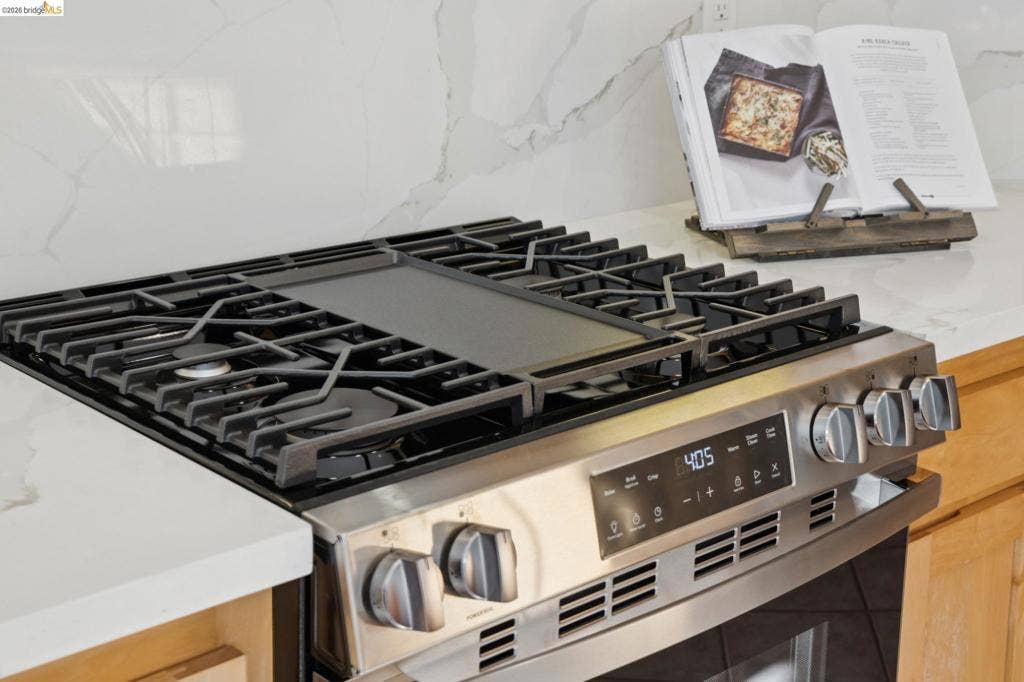 5503 Rainbow Cir, Santa Rosa, CA 95409 Stainless steel gas range with a central griddle, heavy-duty iron burner grates, digital touch controls, and light-toned cabinetry complemented by white stone-finish slab countertops with veining