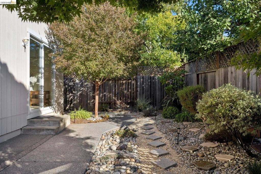 5503 Rainbow Cir, Santa Rosa, CA 95409 Private backyard featuring a concrete patio, stone garden path, decorative rock ground cover, and wood perimeter fencing with lattice top
