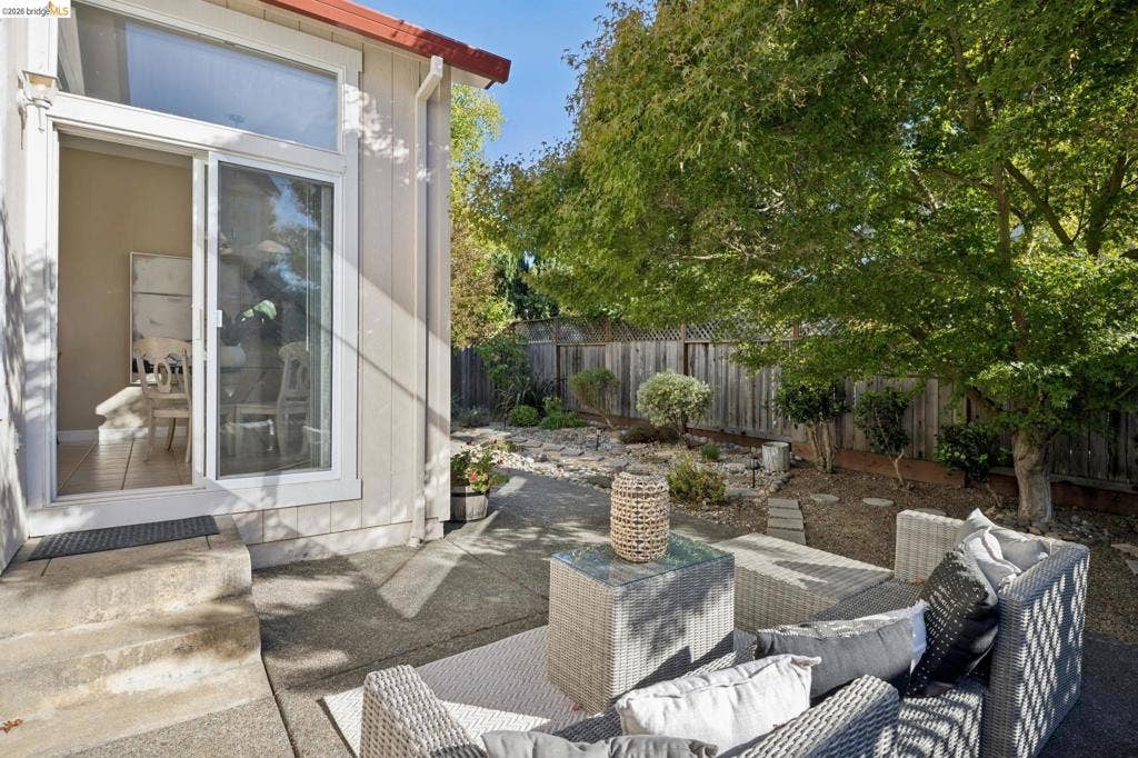 5503 Rainbow Cir, Santa Rosa, CA 95409 Concrete patio featuring a sliding glass door with a transom window, wood-finish privacy fencing, and mature landscape trees