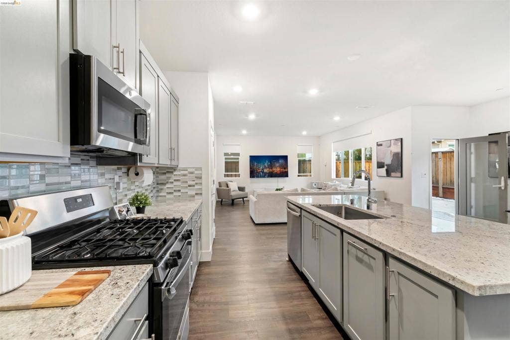 539 Gemstone Way, Oakley, CA 94561 Kitchen featuring shaker-style cabinetry, stone countertops, mosaic tile backsplash, stainless steel appliances, and a center island with an integrated stainless steel sink