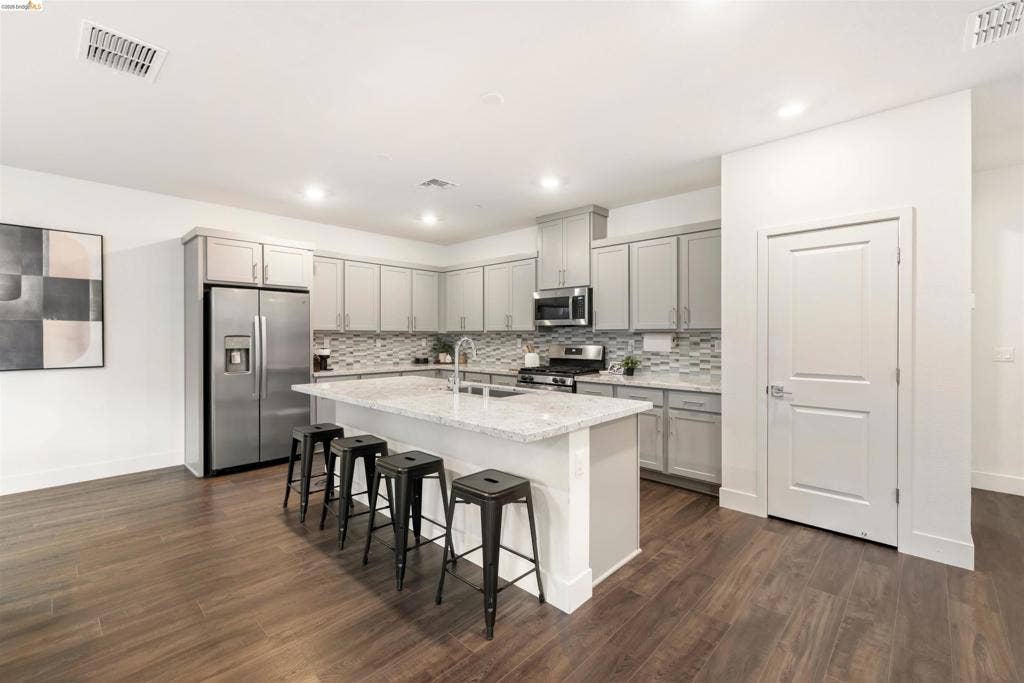539 Gemstone Way, Oakley, CA 94561 Kitchen featuring gray cabinetry, stone-finish countertops, a central island with an integrated sink, stainless steel appliances, and wood-finish flooring